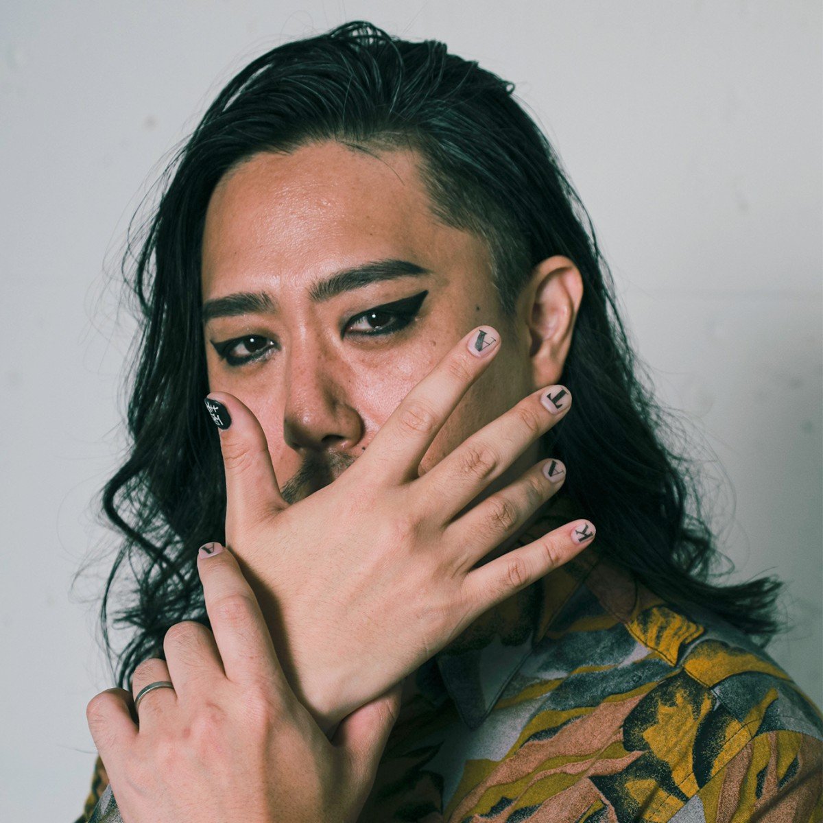 服装・メイク・ヘアスタイルは1枚目と同様。右手は開いて今村の口元を隠しており、ちょうどネイルの「KATA麺」が綺麗に見えている。左手は右手首を軽くにぎっている。