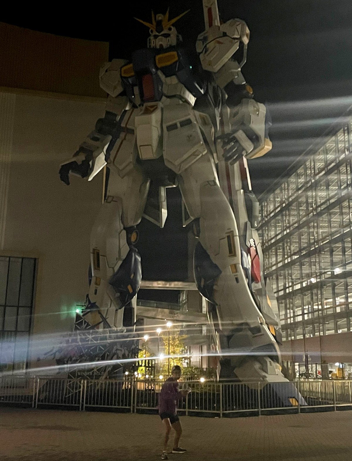 夜のららぽーと、ガンダムの前でポーズを取る新津さん。