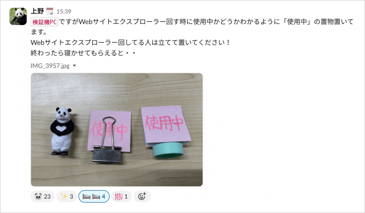 slackのスクリーンショット。上野 検証機 PCですがWebサイトエクスプローラー回す時に使用中かどうかわかるように「使用中」の置物置いてます。 Webサイトエクスプローラー回してる人は立てて置いてください！ 終わったら寝かせてもらえると・・　パンダのフィギュアと、ボトルキャップに「使用中」の紙を取り付けたもの。