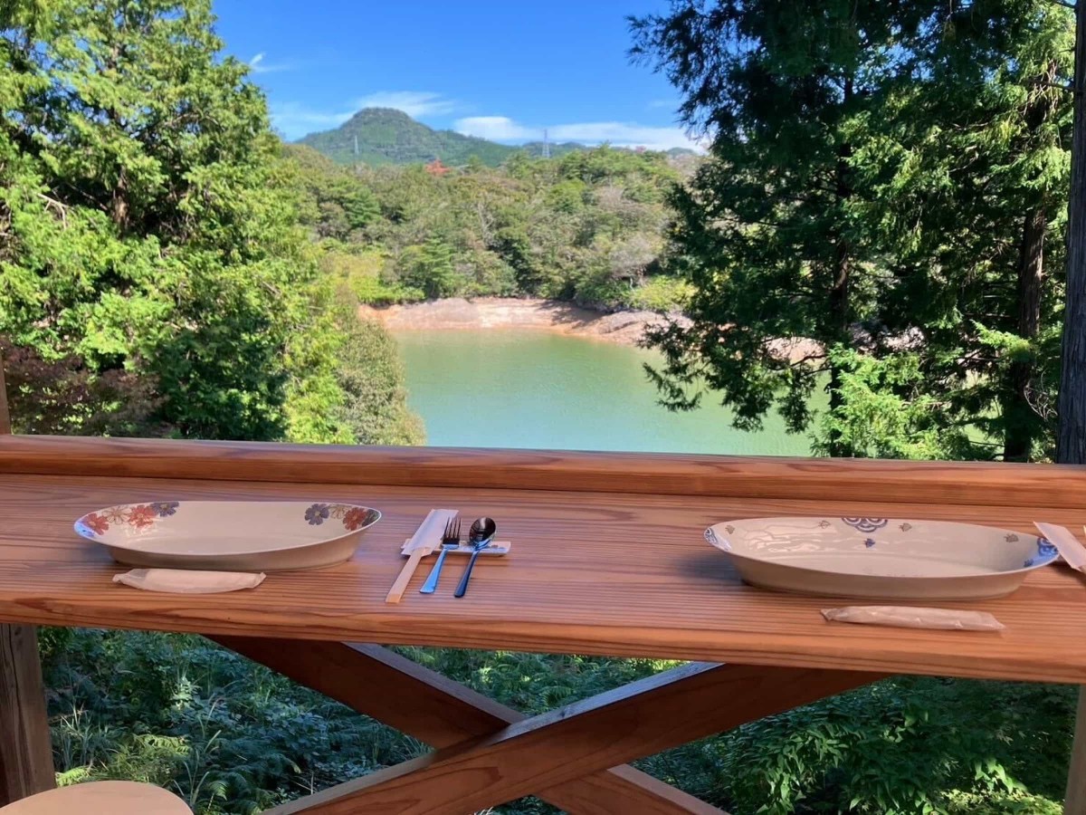 いろえ工房のテラス席から見える風景。木々の向こうに池の水面、さらに向こうには山が見える
