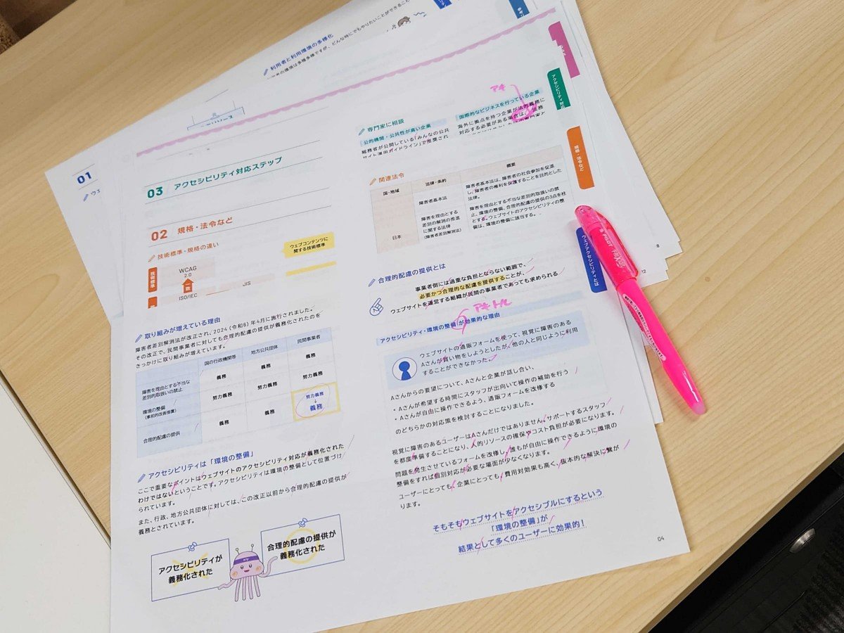 冊子「アクセシビリティってなに？」の最終稿が、机に置かれている画像。ピンクのマーカーで修正点が書き込まれている。