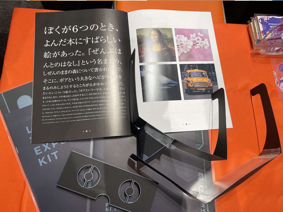 ディーゼロブースのデスクに置かれた「ロービジョン体験キット」の写真。体験メガネと、リーフレットが広げられた状態で置かれている