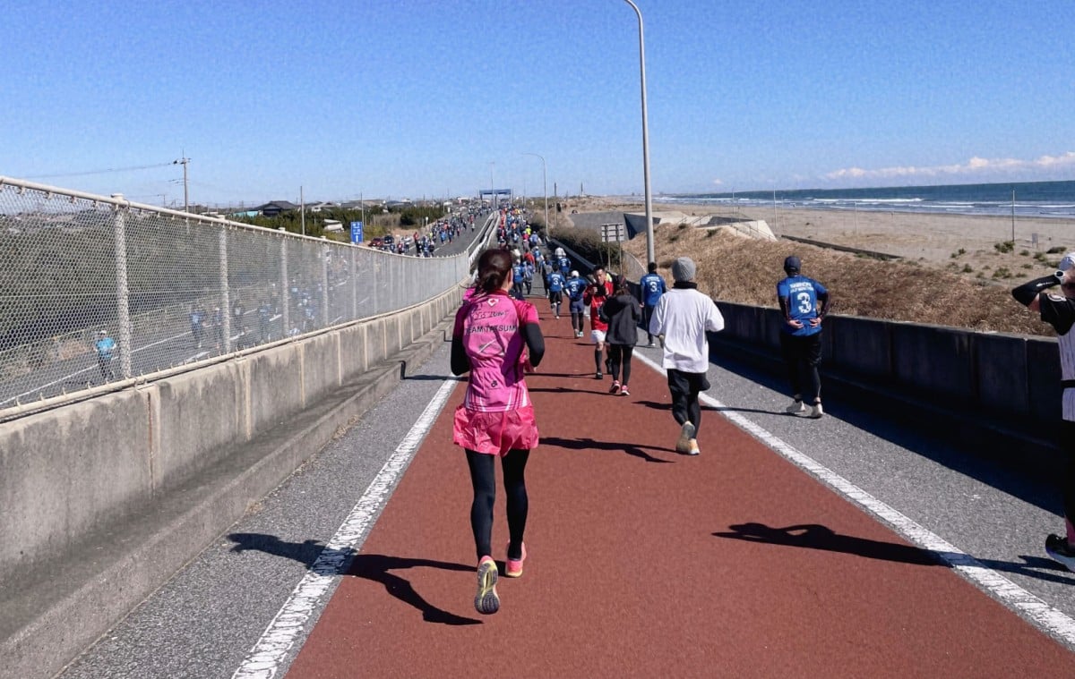 他の参加者とハーフマラソンのコースを走る米田さんの後ろ姿。右手には海岸が見える。