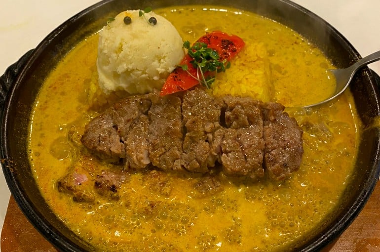 スリランカ風のカレーにポテトサラダと豚ステーキがトッピングされている
