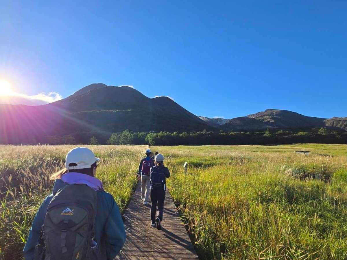 くじゅうの木道を歩いている様子。晴天で青空と山々が行く先に広がっている。