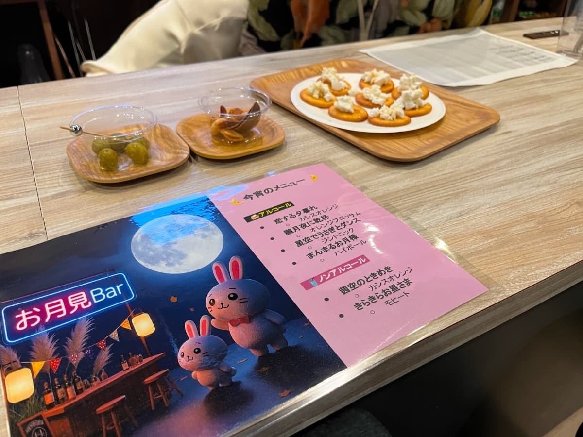 お月見Barのメニューとおつまみ。メニューには今宵のメニューと、満月と白いうさぎとお月見Barのイラストが書かれている。