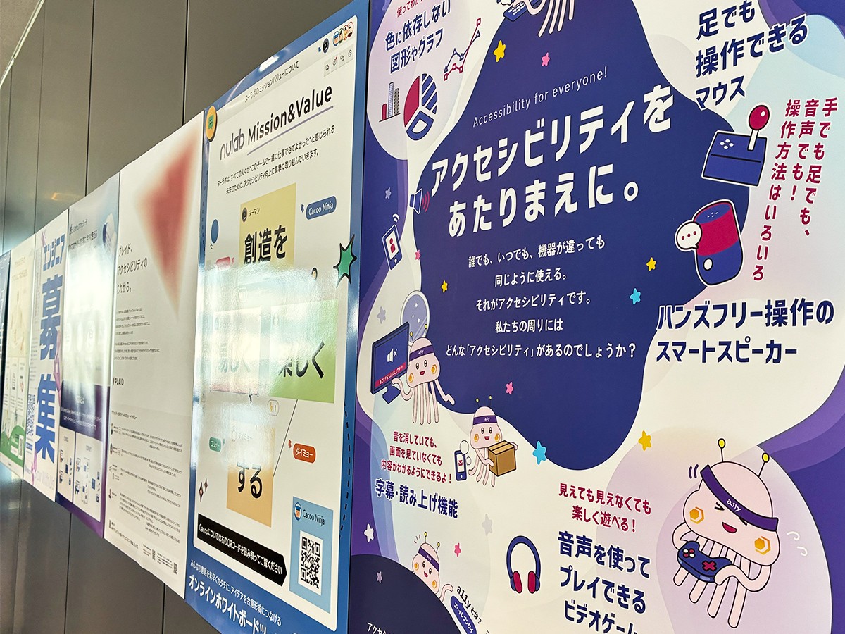 会場内の壁に掲示されたポスター。「アクセシビリティをあたりまえに。」というタイトルのディーゼロのポスターが手前側に、他のポスターは奥側に掲示されている。