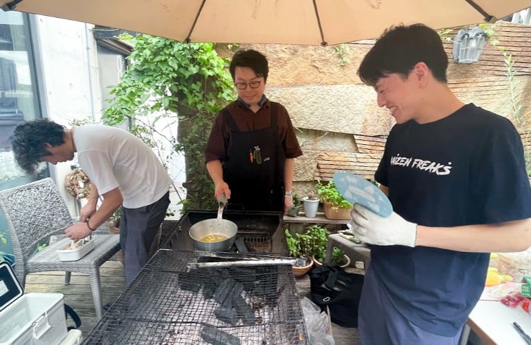 3人の男性が並んでバーベキューの準備をしている。