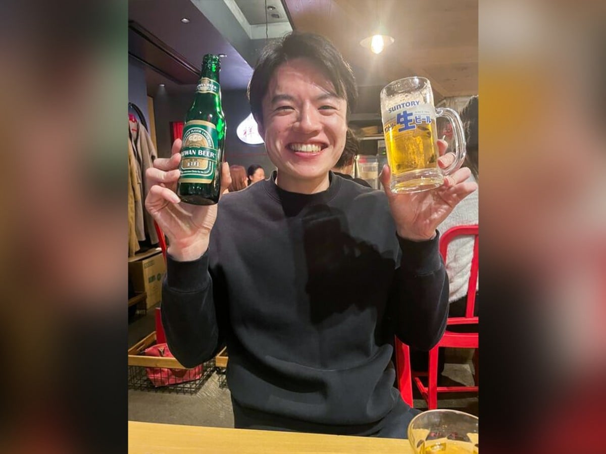 左手にビール瓶、右手にビールグラスを持った小林さんが、笑顔でこちらを向いている。