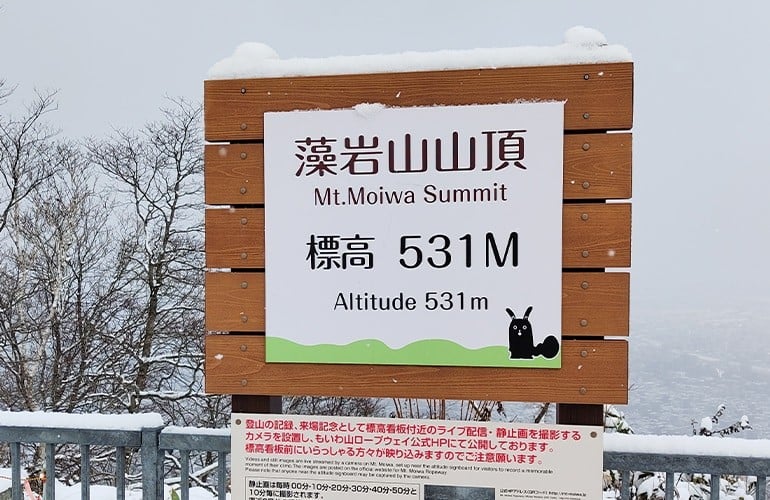 雪の積もった藻岩山山頂の看板の写真。看板には「藻岩山山頂 Mt.Moiwa Summit 標高531M Altitude 531m」と書かれている。