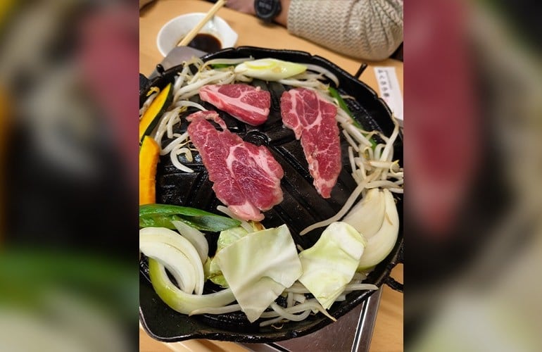 ジンギスカン鍋でジンギスカンと野菜を焼いている様子の写真。 鍋の中央にジンギスカン、その周りにキャベツや玉ねぎなどの野菜が置かれている。