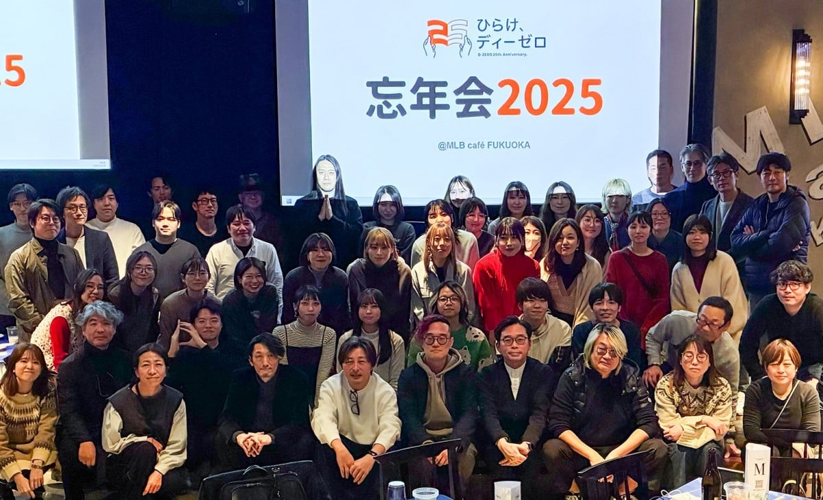 忘年会の集合写真。参加者が「ひらけ、ディーゼロ」のロゴと「忘年会2025」が表示されたスクリーンの前に集まっている。