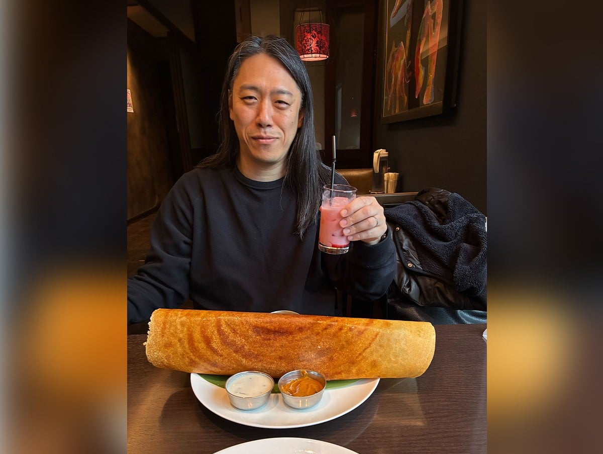 肩幅よりも大きいドーサと飲み物を片手に持った男性の写真。