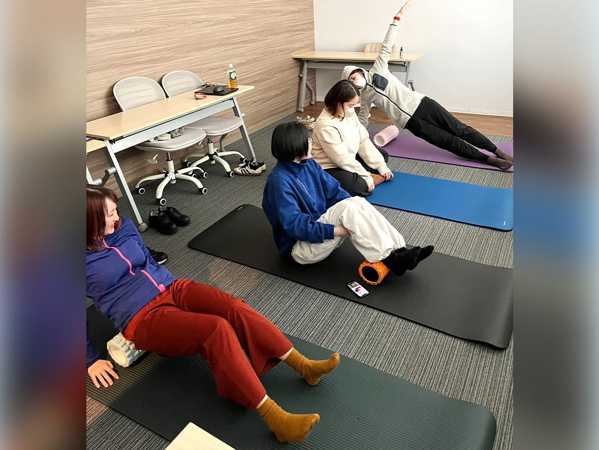 会社の一室でマットを引いてストレッチをしている写真。
