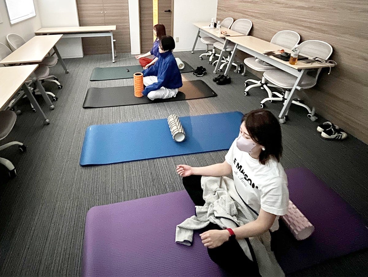 会社の一室でマットを引いてポーズをとっている写真。