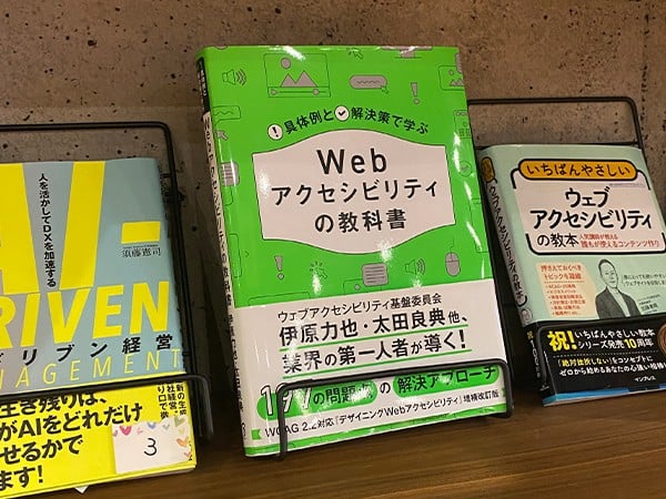 本棚に並ぶ『具体例と解決策で学ぶ Webアクセシビリティの教科書』の表紙