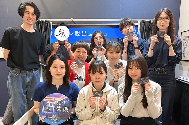 新人メンタープロジェクトメンバーと新人合わせて10人がそれぞれ脱出ゲームのカードと脱出失敗と書かれたパネルを持っている記念写真。