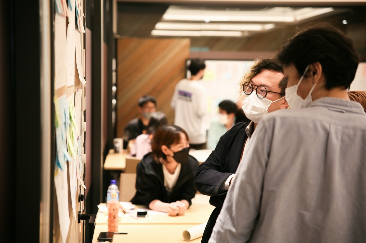 写真: ホワイトボードに貼ったワークショップの結果を眺めながら会話をする参加者