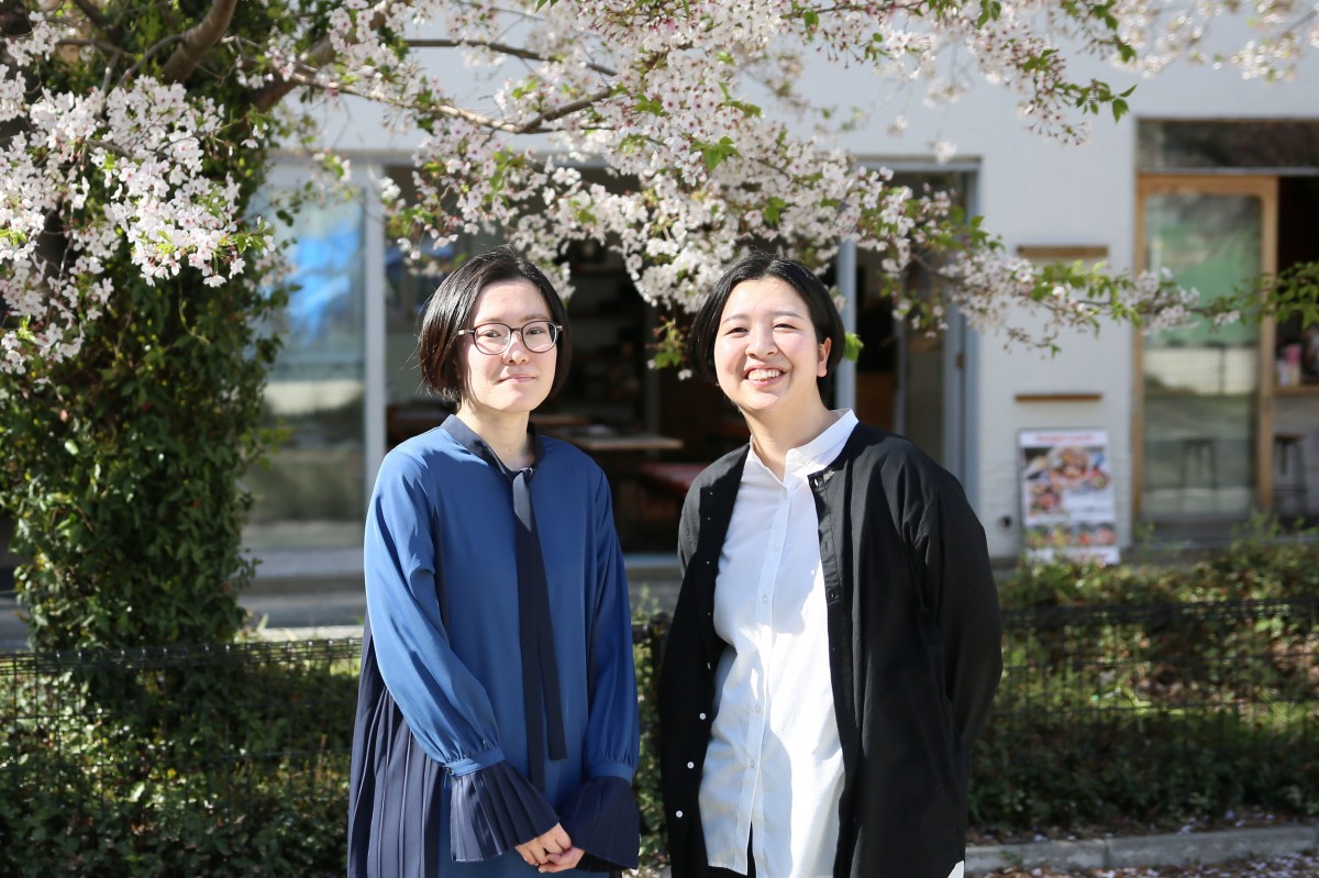 桜の木の下で新卒2人が笑っている写真